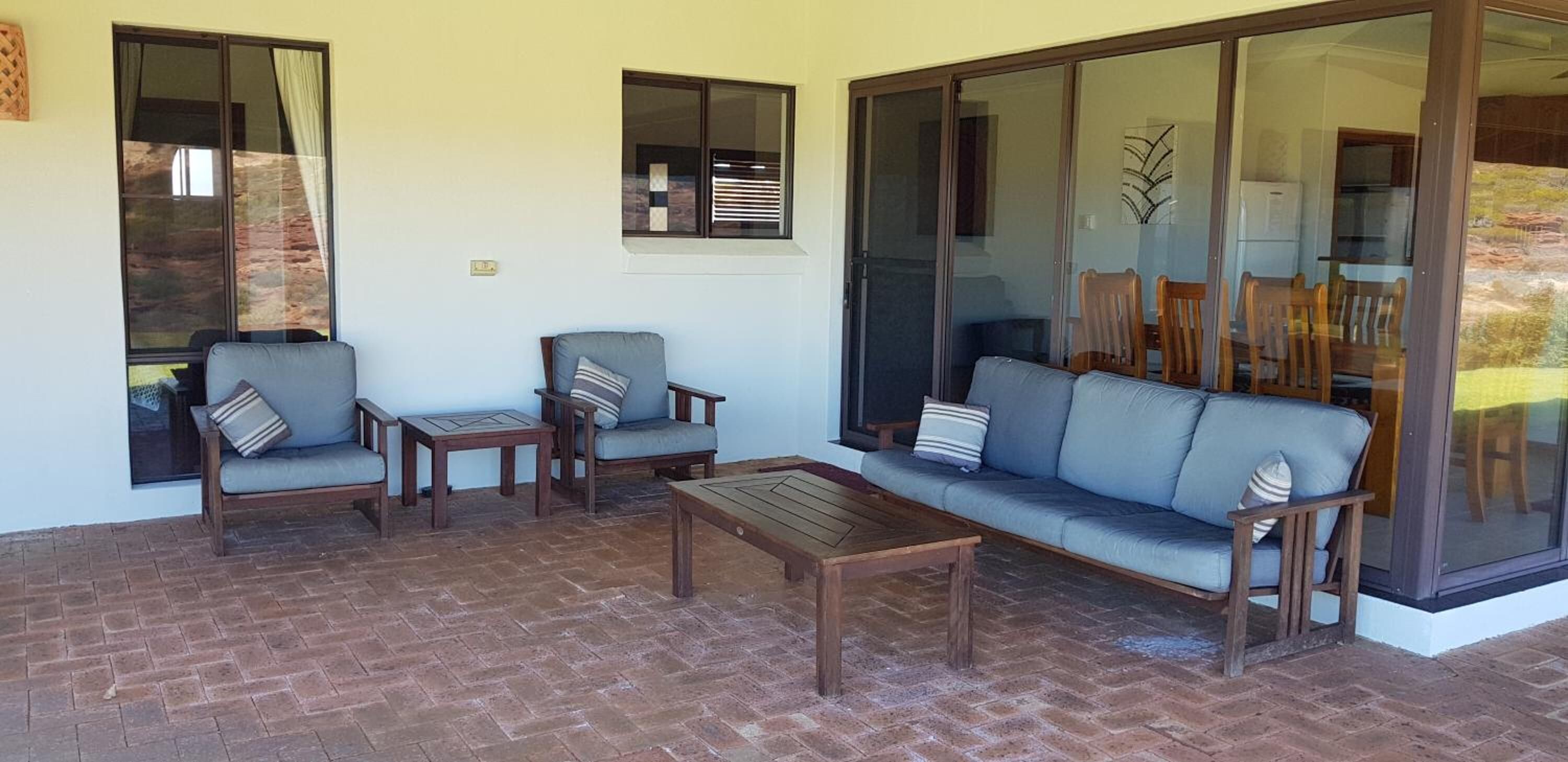 Un espacio de patio con un sofá, dos sillones, una mesa y un ventanal de vidrio que da a un comedor.
