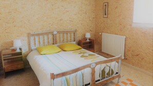 A bedroom with a wooden bed, yellow pillows, a white radiator, and a checkered rug. - house in farmhouse (saint nectaire)