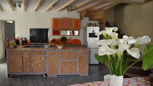 A kitchen with wooden cabinets, a white refrigerator, and a dining area with a table covered by a floral tablecloth. - house in farmhouse (saint nectaire)