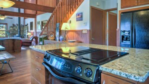 A kitchen with a built-in stove, granite countertop, wooden cabinets, and a stone fireplace.