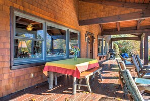 Une terrasse en bois avec une table et des bancs, de grandes fenêtres et un espace couvert aménagé avec des sièges.