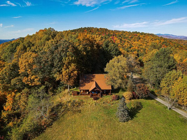 Un chalet entouré d’un feuillage automnal, offrant une vue dégagée sur la forêt environnante et les montagnes lointaines.