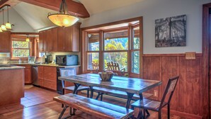 A kitchen with wooden cabinets, a dining table with benches, and a large window with a view of trees.