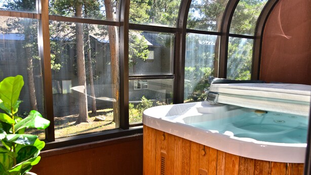 Ein Whirlpool mit Holzverkleidung, nahe einem großen Fenster mit Blick auf einen Garten mit Bäumen und einem Haus.