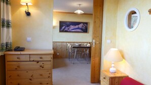 Een kamer met een houten dressoir, een rode bank, een lamp, een eettafel met stoelen, een schilderij aan de muur en een spiegel.