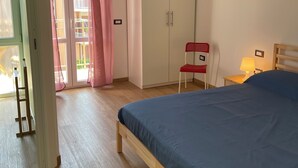 A bedroom with a wooden bed, a wardrobe, a chair, and a balcony with pink curtains.