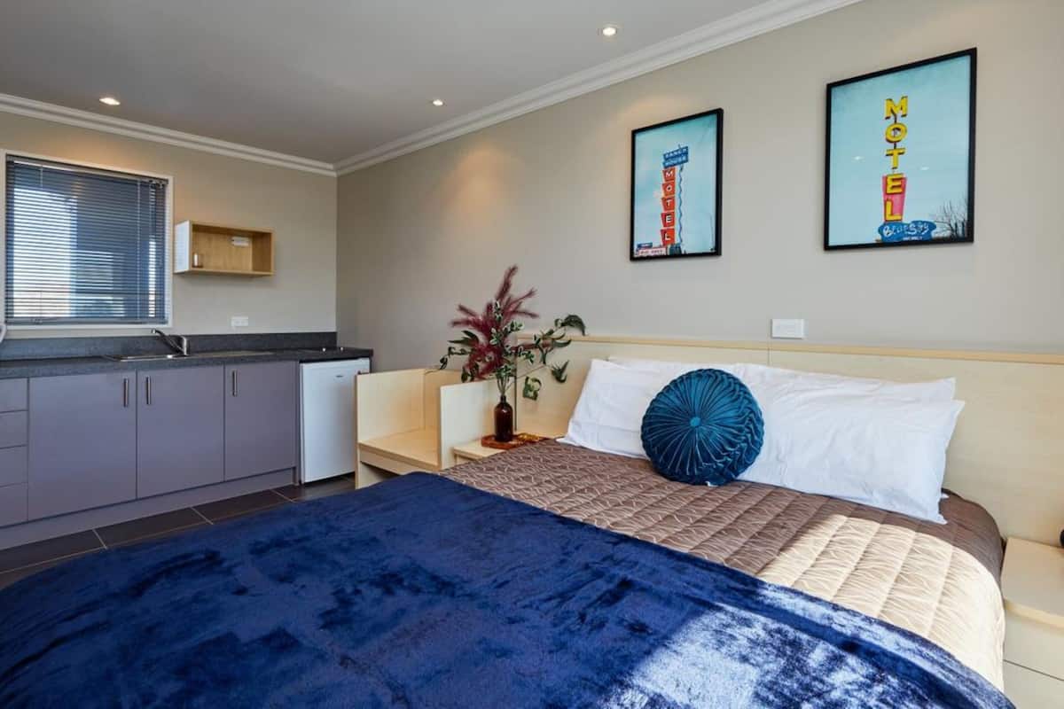 A bedroom with a bed, a nightstand, a potted plant, and a wall-mounted TV.