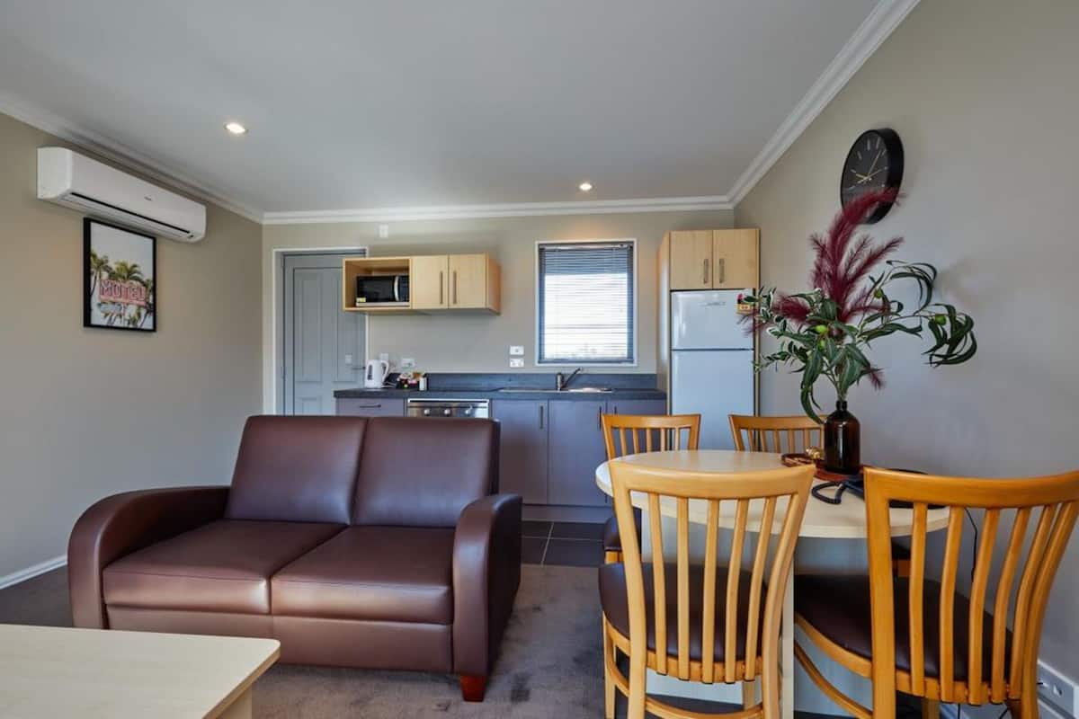 A compact living space with a sofa, dining table, chairs, kitchenette, and a decorative plant.
