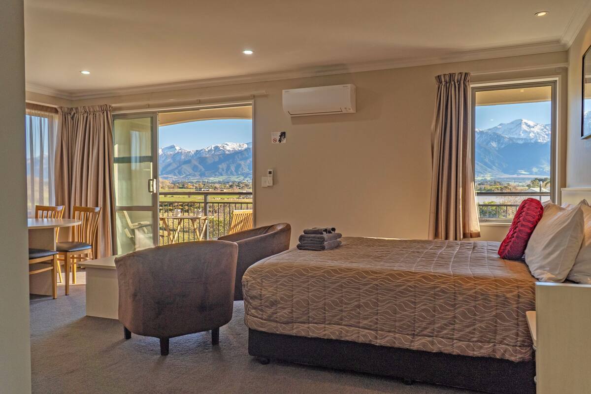 A hotel room with a bed, a chair, a table, and a balcony with a mountain view.
