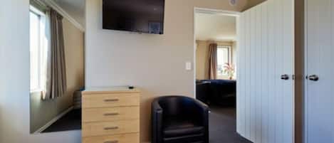 A hotel room with a wooden dresser, a black chair, a television mounted on the wall, and a large wardrobe.