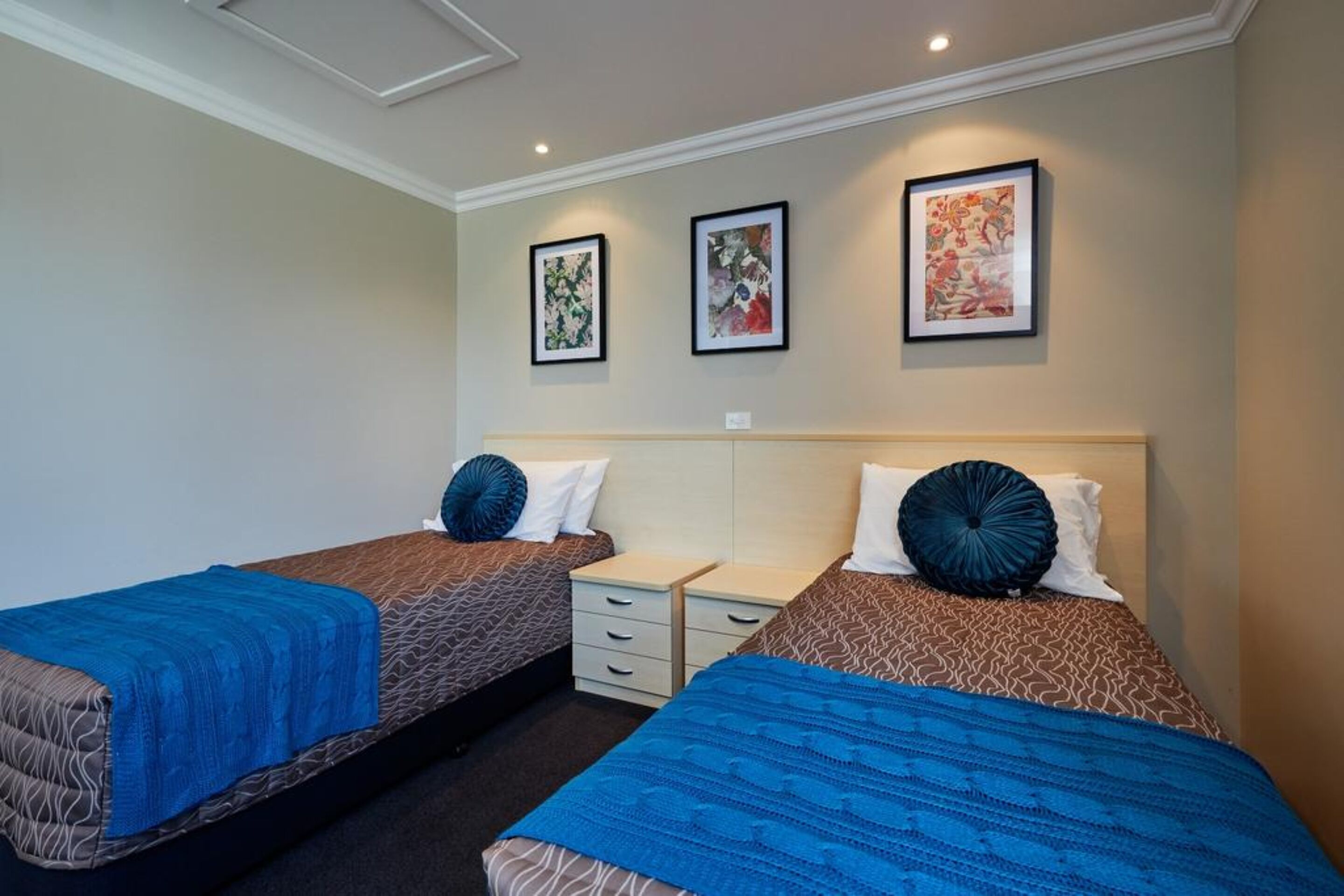 Habitación de hotel con dos camas, cada una con una manta azul, almohadas blancas y cabecero. Hay tres obras de arte enmarcadas en la pared.