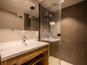 A modern bathroom with a wooden vanity, a glass shower enclosure, and a large mirror.
