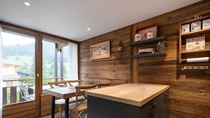 A modern kitchen with wooden accents, a dining area with wooden chairs, and a view through a glass door.