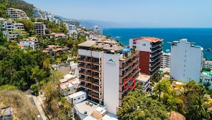 Un hotel sulla costa con diversi edifici, tra cui un edificio bianco caratteristico con balconi e una zona piscina sul tetto.