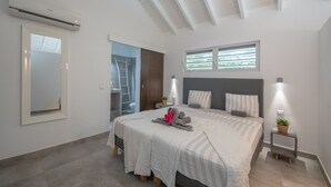 Ein modernes Schlafzimmer mit einem großen Bett, einem Deckenventilator, einem Fenster mit Jalousien und einem kleinen Nachttisch mit Lampe.
