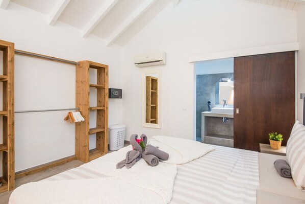 Une chambre moderne avec un lit, des étagères en bois, une salle de bain avec un miroir et une plante.