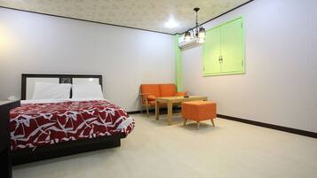 Quarto de hotel com cama, uma mesinha, duas cadeiras e um armário verde.