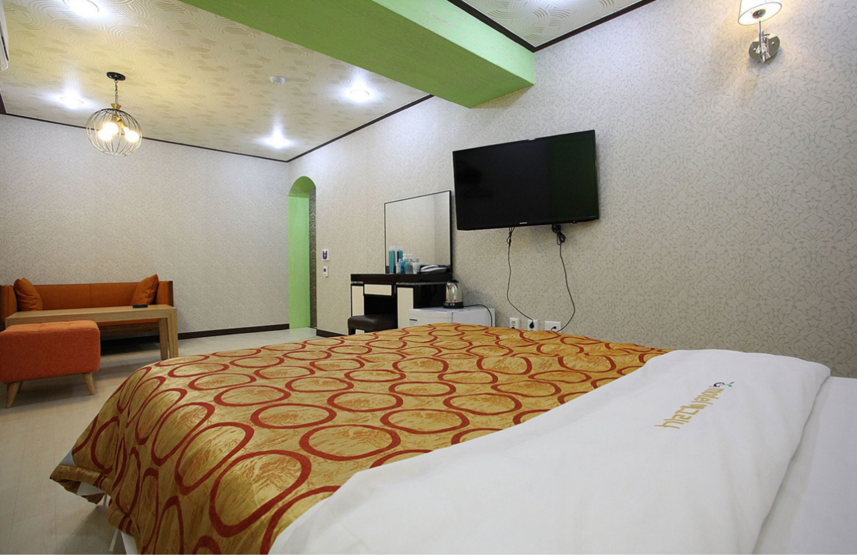 Een hotelkamer met een groot bed, een aan de muur bevestigde televisie, een bureau met stoel en een bank.