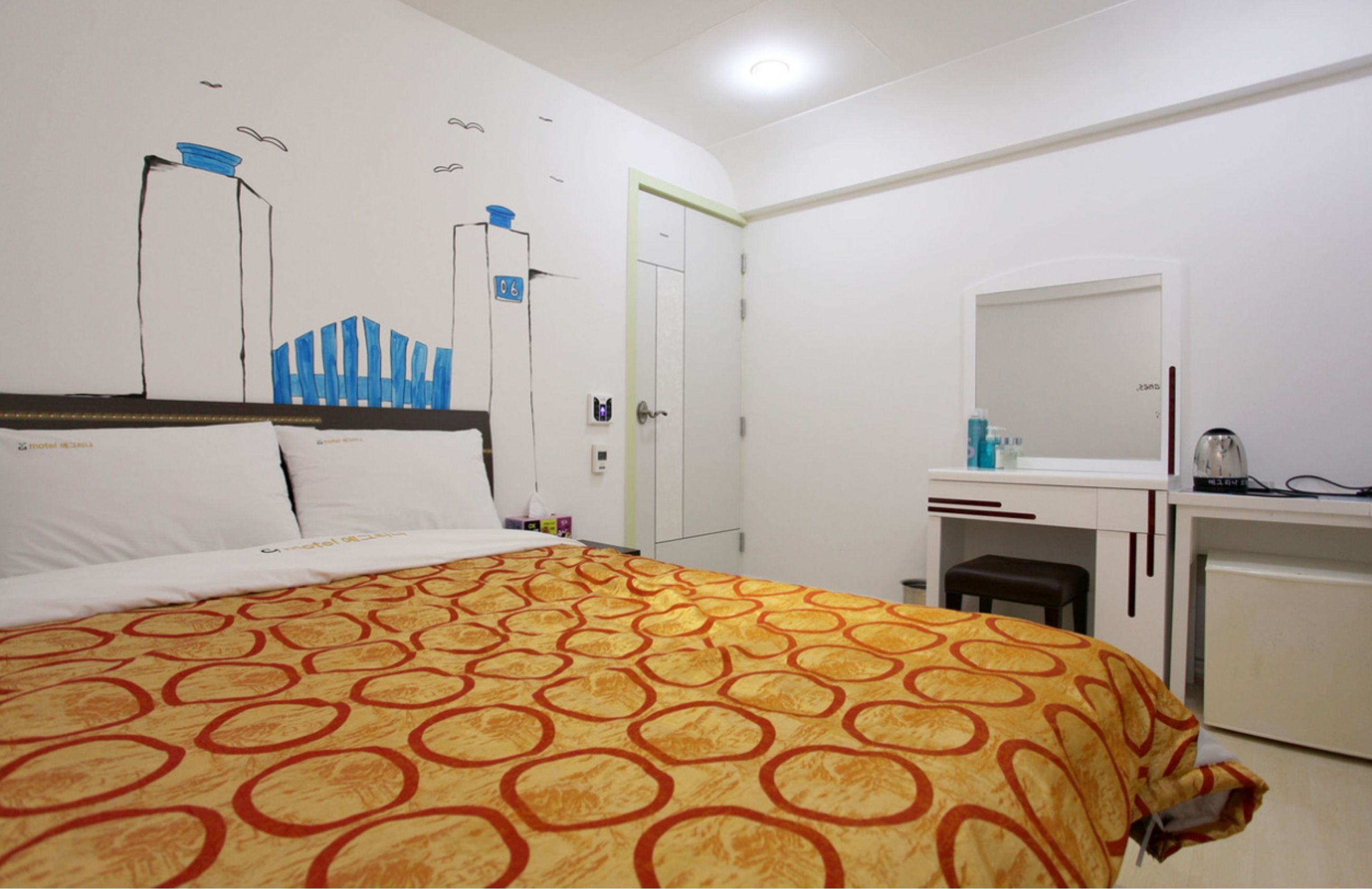 A hotel room with a bed, a desk, a chair, a mirror, and a wardrobe.