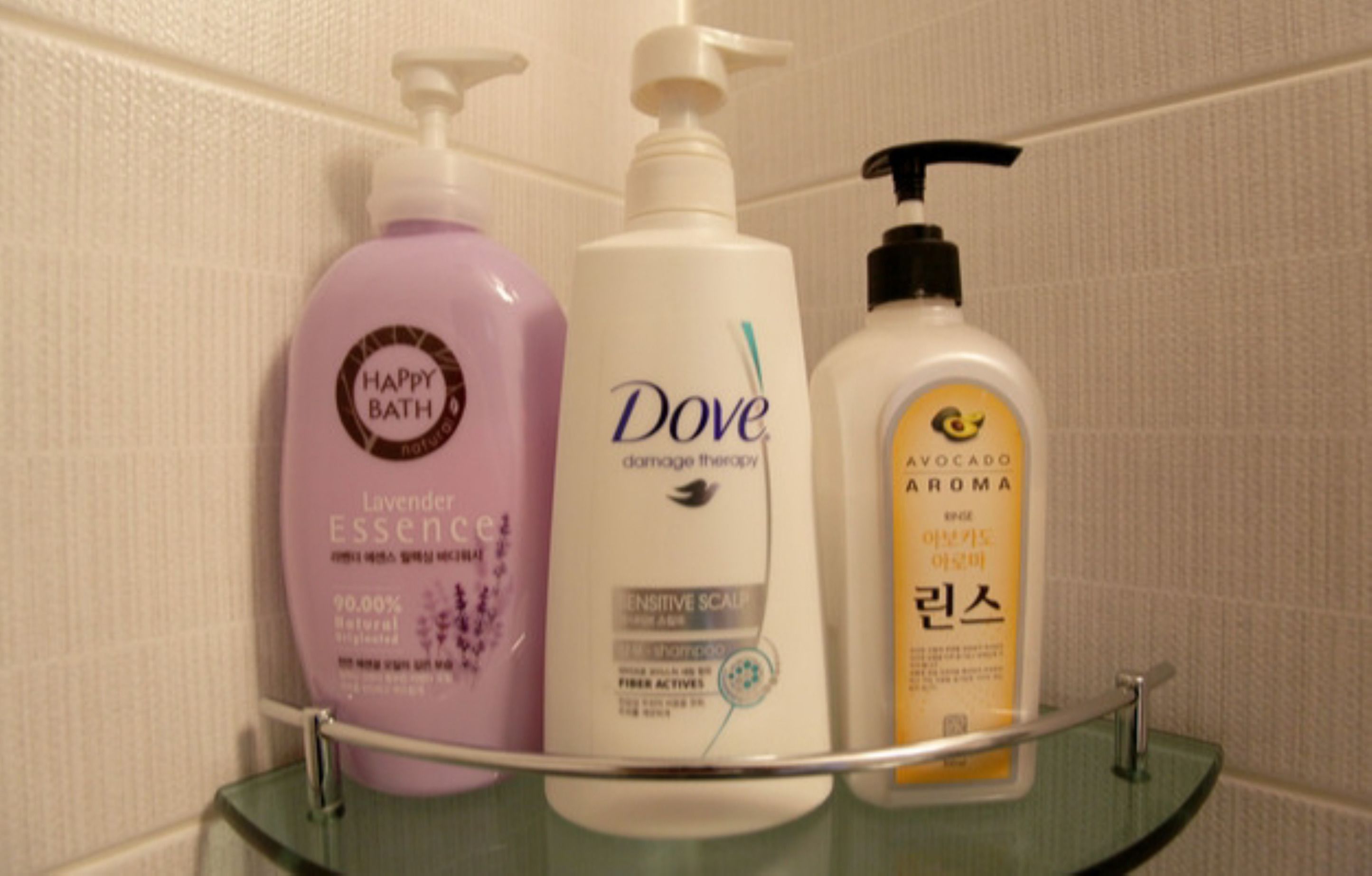 Three bottles of toiletries on a glass shelf in a bathroom.