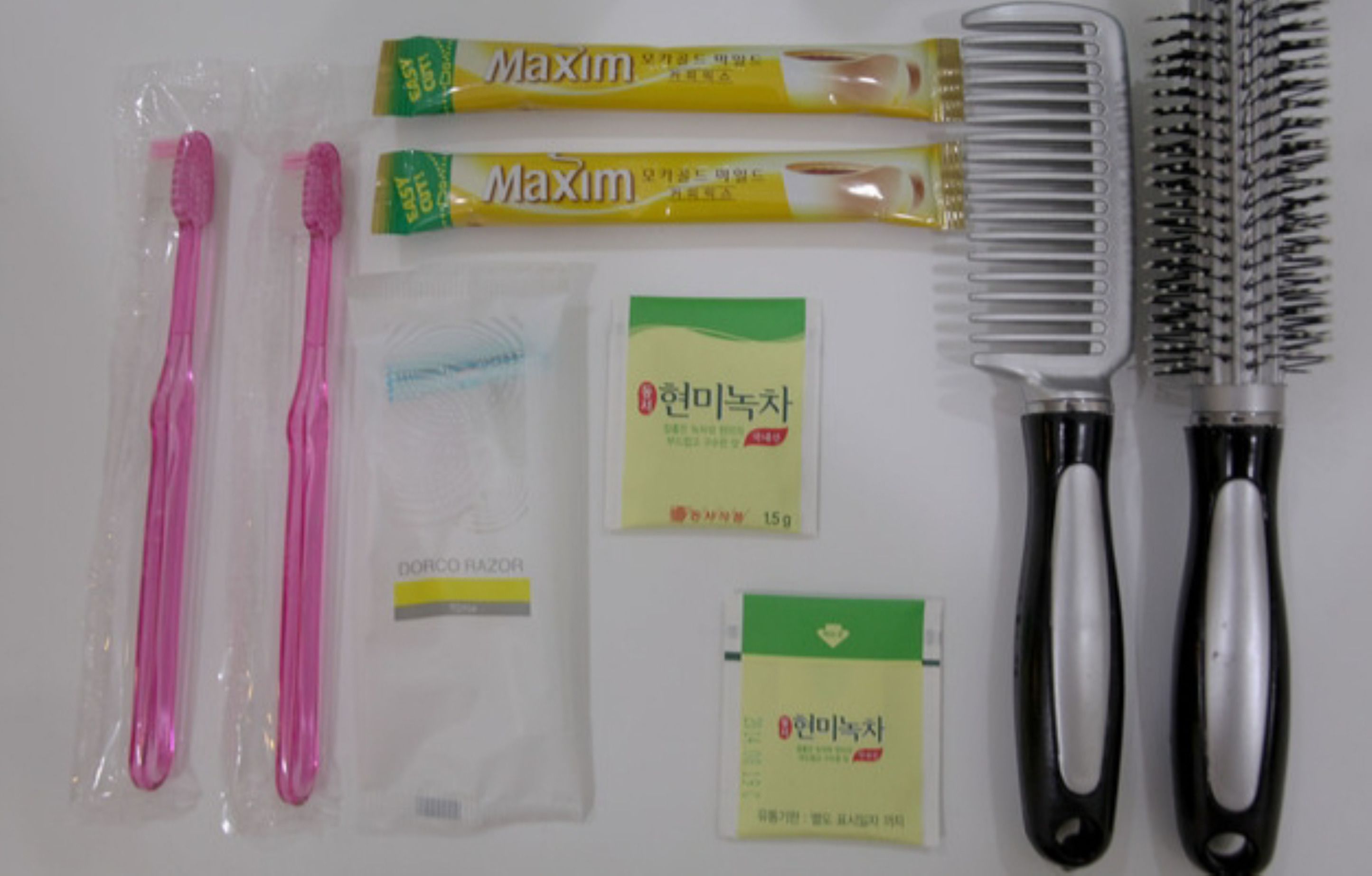 Un ensemble de produits d’hygiène personnelle comprenant deux brosses à dents roses, deux tubes de dentifrice Maxim, un peigne, une brosse à cheveux et deux petits échantillons de produits pour les soins capillaires.