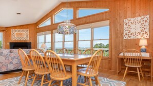 Un intérieur en bois comprenant une table à manger, des chaises, une cheminée et de grandes fenêtres donnant sur un paysage.