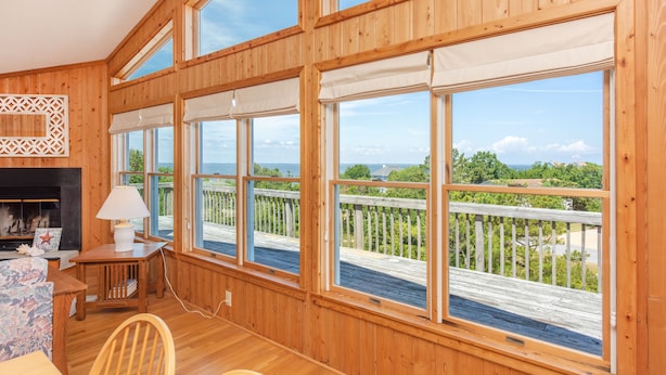 Un intérieur en bois, doté de grandes fenêtres, d’une cheminée et offrant une vue sur une terrasse en bois et sur la verdure.