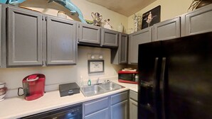 Eine Küche mit grauen Schränken, einem schwarzen Kühlschrank, einer roten Kaffeemaschine, einer Mikrowelle und einem Geschirrspüler.
