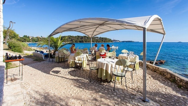 Un espace de restauration en plein air avec des tables et des chaises, un coin salon abrité et une vue sur la mer.