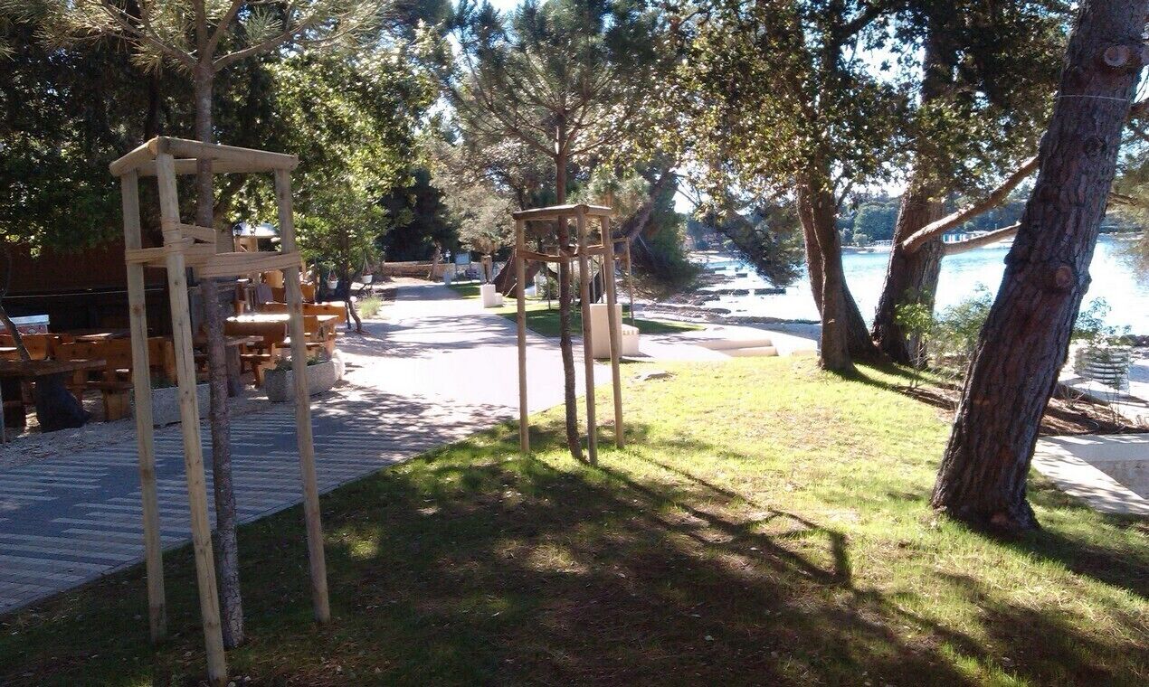 An outdoor area with wooden structures, a paved walkway, and a body of water in the background.