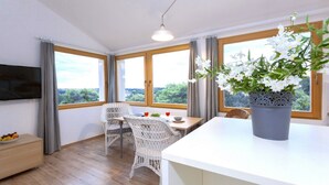 Une pièce moderne comprenant une table à manger, des chaises en osier, une grande plante en pot et un téléviseur à écran plat fixé au mur.