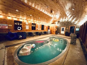 An indoor swimming pool with a wooden interior, a lifeguard on duty sign, and a few chairs and tables.