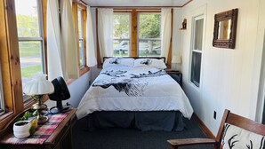 Une chambre à coucher avec un lit, une table de chevet avec une lampe, une chaise et une fenêtre avec des rideaux.