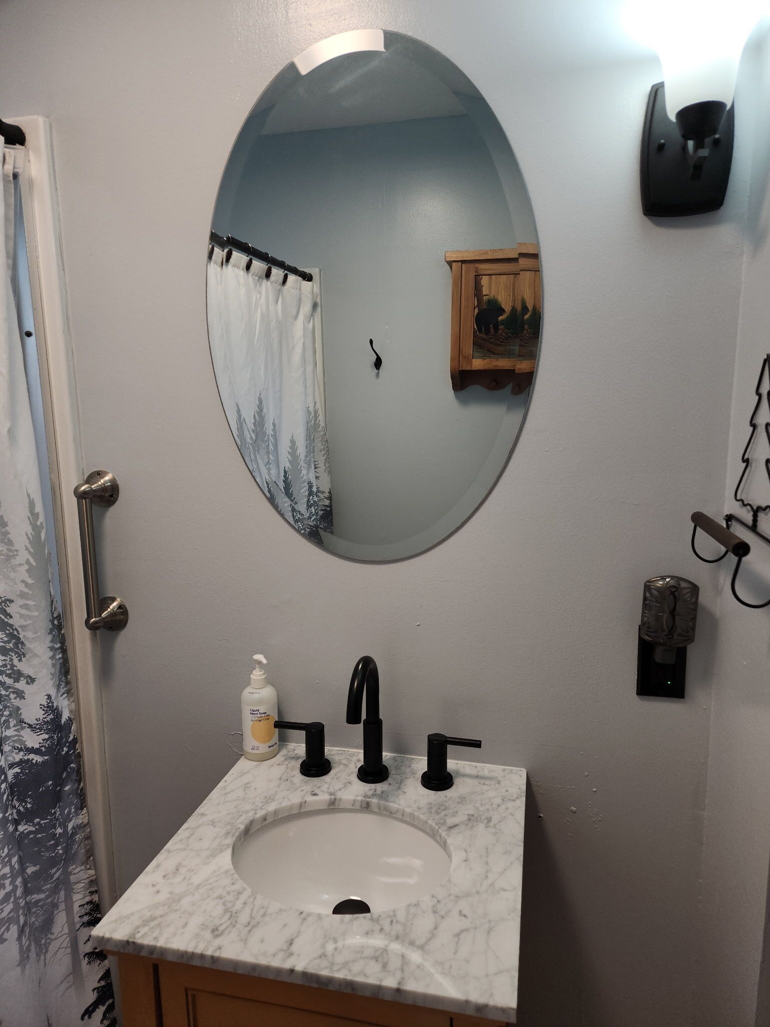 A bathroom with a round mirror, a sink with a marble countertop, a shower curtain, and a small wooden decoration on the wall.