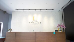 A hotel reception desk with a logo, a flower vase, and a sign indicating a 24-hour service.