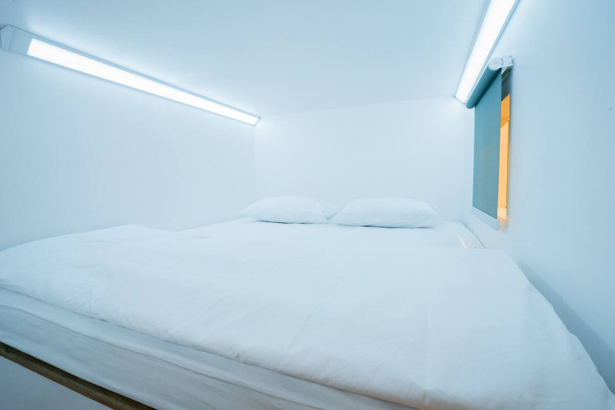 Een minimalistische slaapkamer met een bed, witte muren en een plafondlamp.