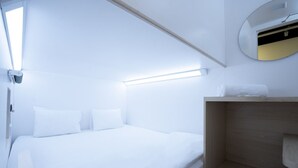 A modern, minimalist hotel room with a neatly made bed, a wooden vanity, and a round mirror on the wall.