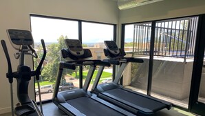 Un gimnasio con cintas de correr y una máquina elíptica, amplias ventanas con vistas al exterior.