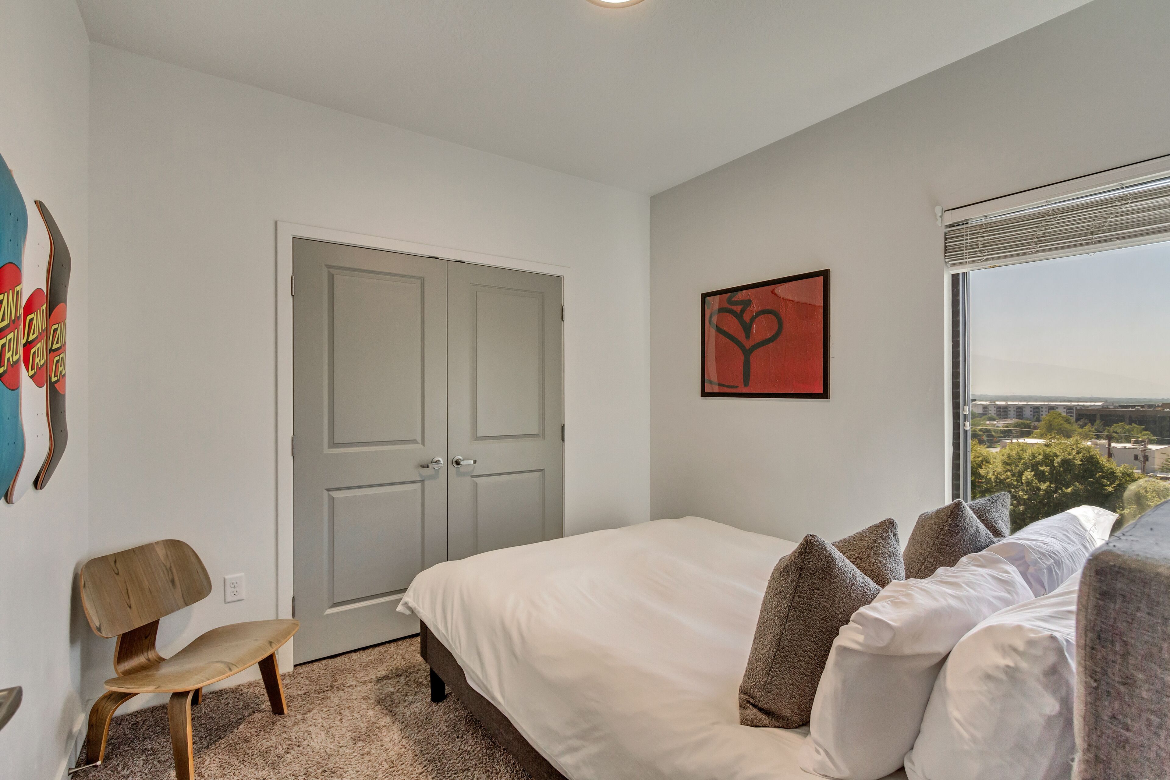 A bedroom with a bed, a chair, a door, and a window with a view.