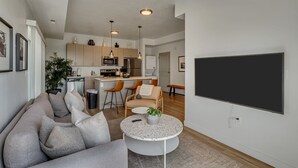 Una sala de estar moderna con un sofá gris, una mesa redonda de centro y un televisor de pantalla plana montado en la pared.