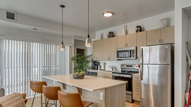 Una cocina moderna con una isla central, electrodomésticos de acero inoxidable, armarios de madera e iluminación colgante.