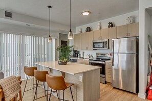 A modern kitchen with a central island, stainless steel appliances, wooden cabinets, and pendant lighting.
