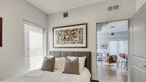 Un dormitorio con una cama grande, una obra de arte floral enmarcada sobre la cama, y vistas al área de estar contigua.
