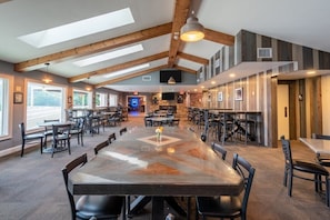 A spacious dining area with high ceilings and exposed beams, featuring multiple tables and chairs.
