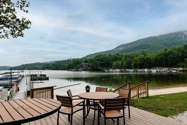Terraza junto al lago con una mesa y sillas, un muelle y vistas a un lago y colinas boscosas.