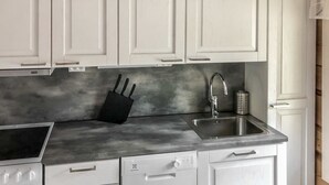 Une cuisine avec des meubles blancs, un évier en acier inoxydable, un bloc à couteaux noir et un lave-vaisselle.