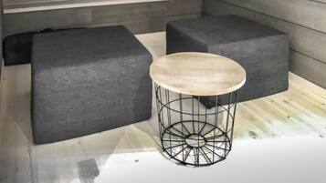 Una habitación con piso de madera, una mesa redonda con estructura de alambre y dos sofás grises tapizados.