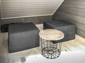 Una habitación con piso de madera, una mesa redonda con estructura de alambre y dos sofás grises tapizados.