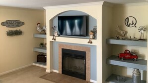 Ein Wohnzimmer mit Kamin, einem Wand-Fernseher und Dekorationen auf Regalen.