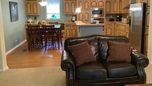 Ein Wohnzimmer mit Ledersofa, Essbereich mit Holzsesseln und eine Küche mit Küchenschränken aus Holz und Edelstahlgeräten.